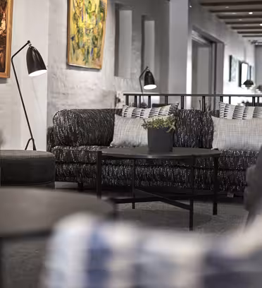 Koselig, moderne salong med mørke sofaer, svarte metallbord toppet med små potteplanter. Veggkunst dekorerer de hvitmalte murveggene. Myk belysning og et tretak skaper en innbydende atmosfære.